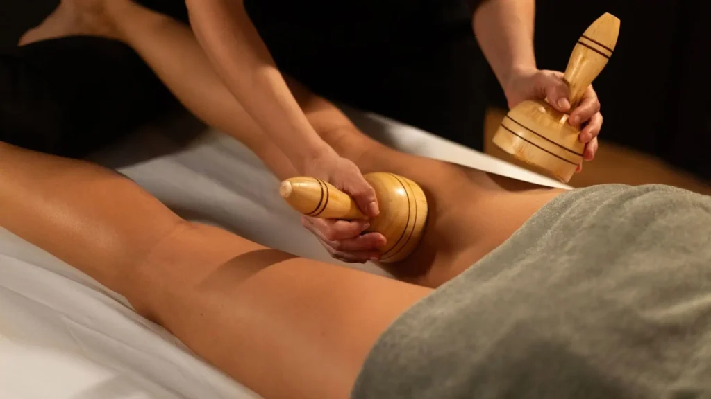 Profesional de estética realizando un tratamiento de maderoterapia corporal con rodillo estriado para reducir la celulitis.